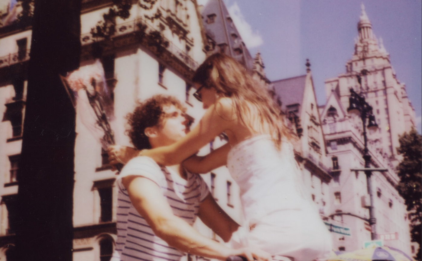 Joshua holding onto a woman's waist while sitting on a bike in front of a castle scenery.